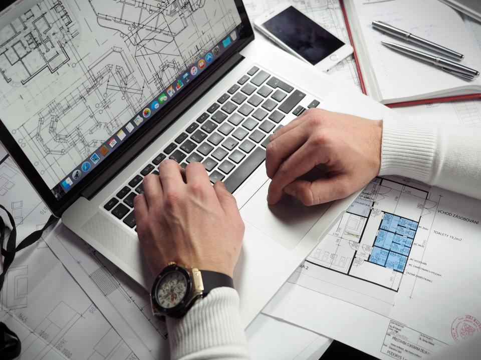 Designer reviewing floor plans on a laptop and paper drawings