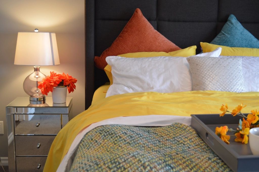 Bed with a dark headboard, yellow and orange cushions and a lamp with flowers