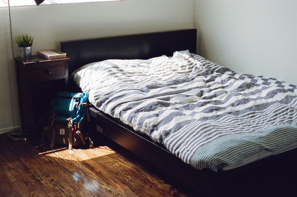 Simple small bedroom with a dark wooden bed and sunlight on the floor